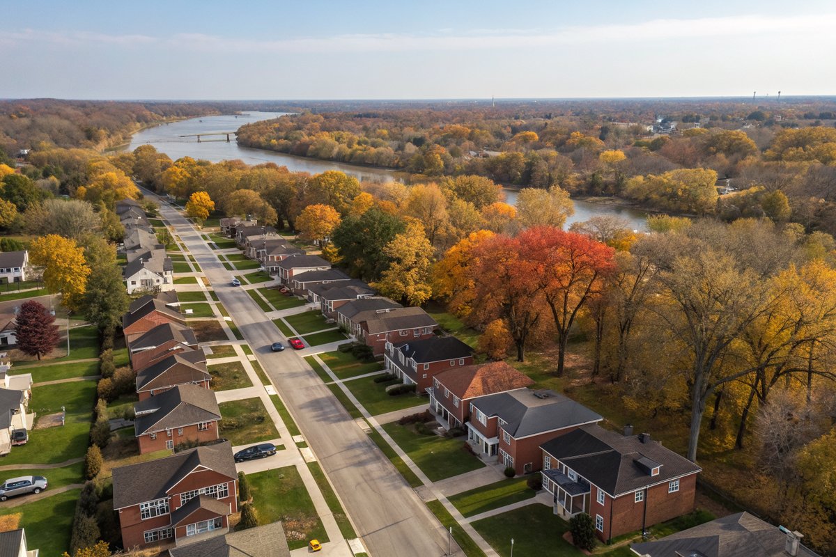 Aerial view of tree-lined streets of older brick houses beside a winding river in autumn
